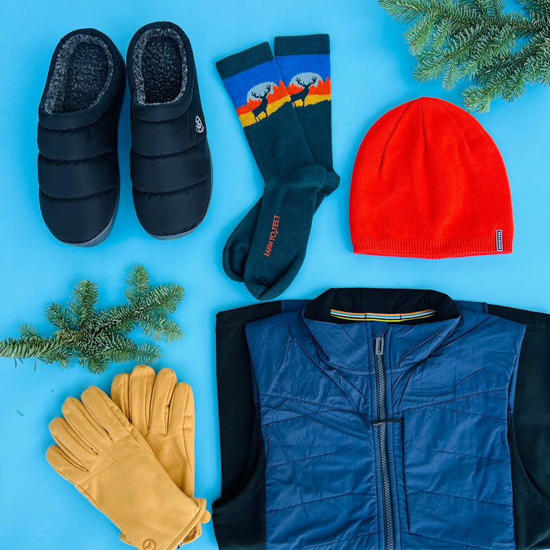 A flat lay of gifts for men, including a pair of slippers, socks, gloves, hat, and vest